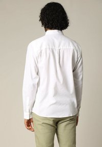Chemise blanche à manches longues en tissu léger, dotée d'un empiècement au dos, d'un ourlet arrondi et de poignets boutonnés, associée à un pantalon vert clair.