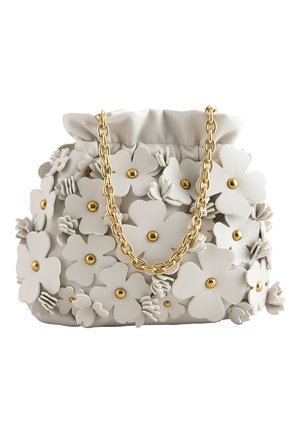 Junge Frau mit langen dunklen Haaren trägt ein hellgelbes Spitzenkleid und hält eine weiße Handtasche, die mit großen Blumenapplikationen und goldenen Perlen verziert ist.