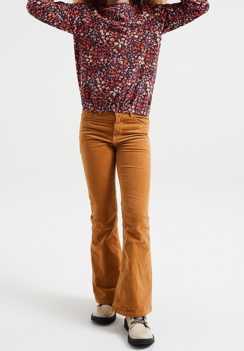 Kwiatowa bluzka z długim rękawem w kolorze granatowym z czerwonymi i białymi kwiatami; zestawiona z jasnobrązowymi spodniami z sztruksu w fasonie dzwonów; masywne beżowe botki z czarnymi sznurówkami.