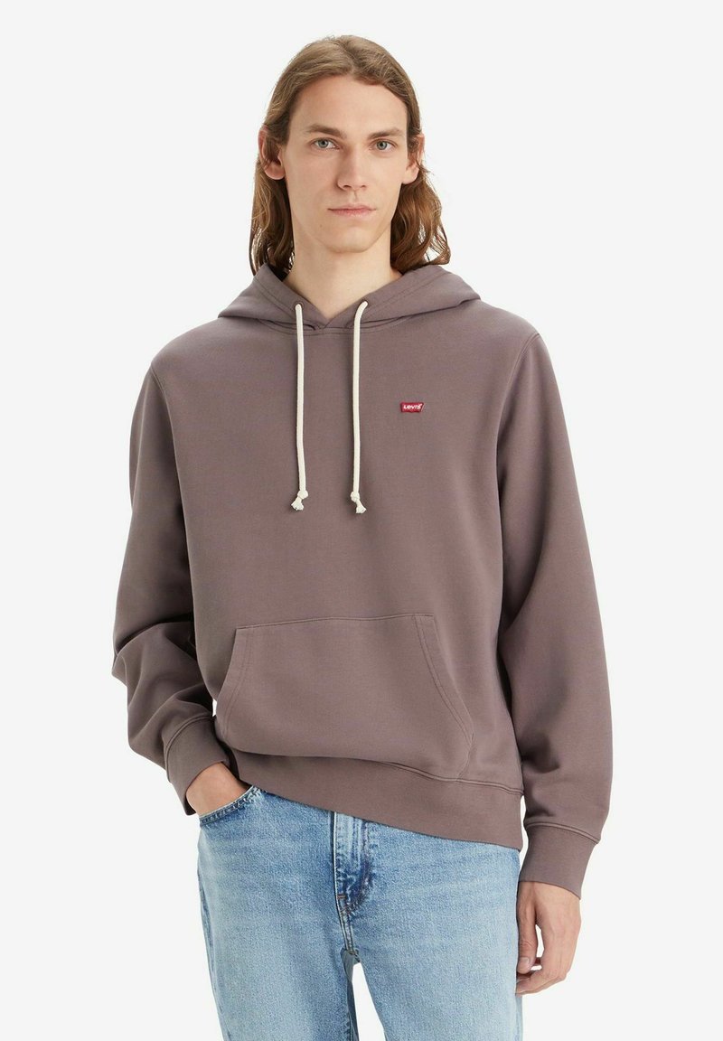 Felpa con cappuccio viola, dotata di tasca frontale e lacci beige. Presenta un piccolo logo rosso sul petto. Indossata con jeans azzurri chiari.