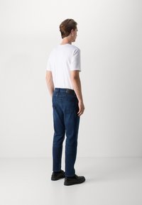 Jeans in denim blu scuro con taglio dritto, dotati di una cintura nera e due tasche posteriori. Abbinati a una t-shirt bianca semplice e scarpe nere.