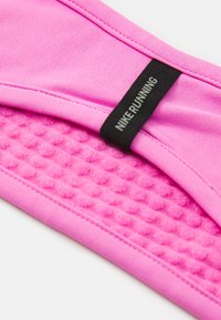 Roza Nike trkačka oprema od mekog materijala, sa teksturiranim panelom i crnom oznakom s natpisom "NIKE RUNNING".