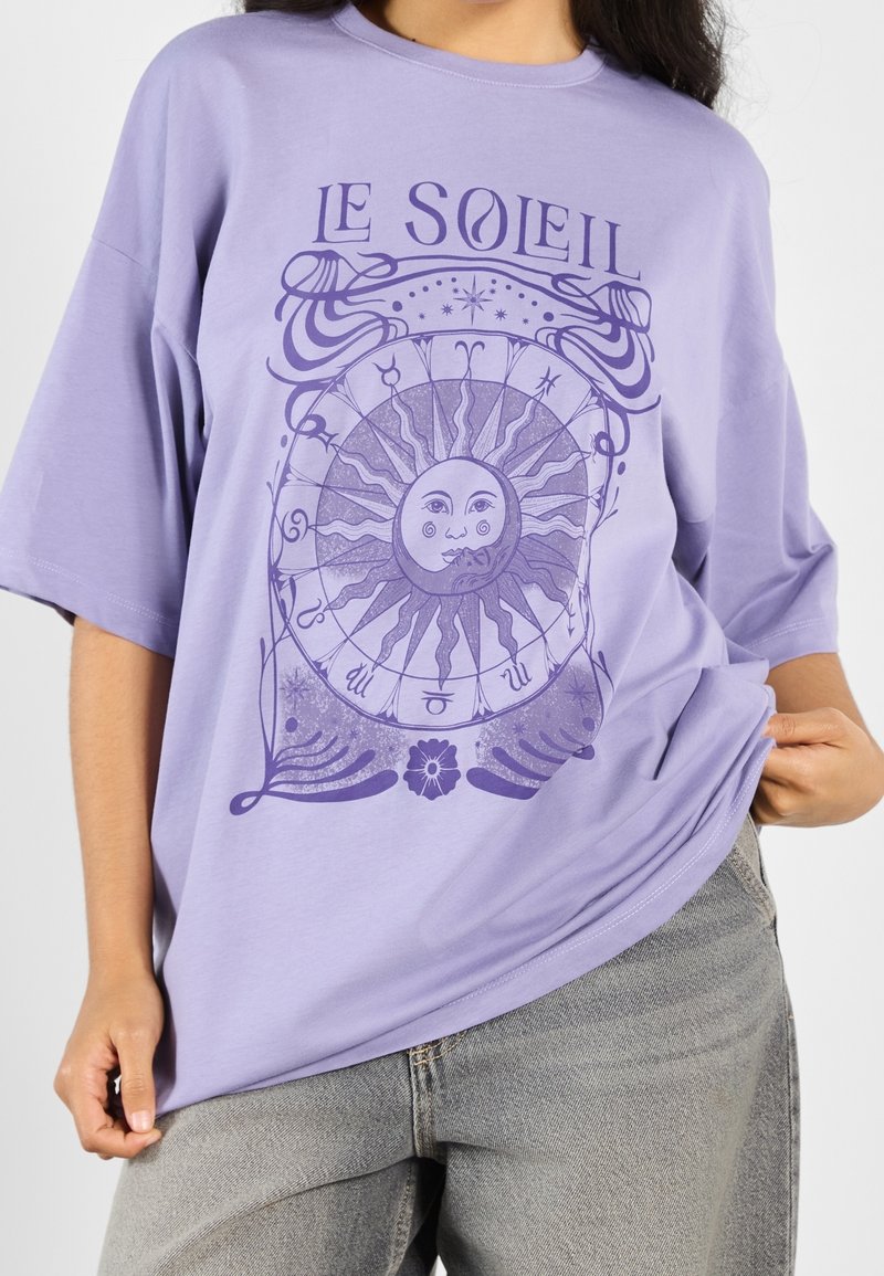 Camiseta oversized morada con un gráfico del sol con detalles intrincados y el texto "LE SOLEIL" en un tono más oscuro. Material de algodón suave.
