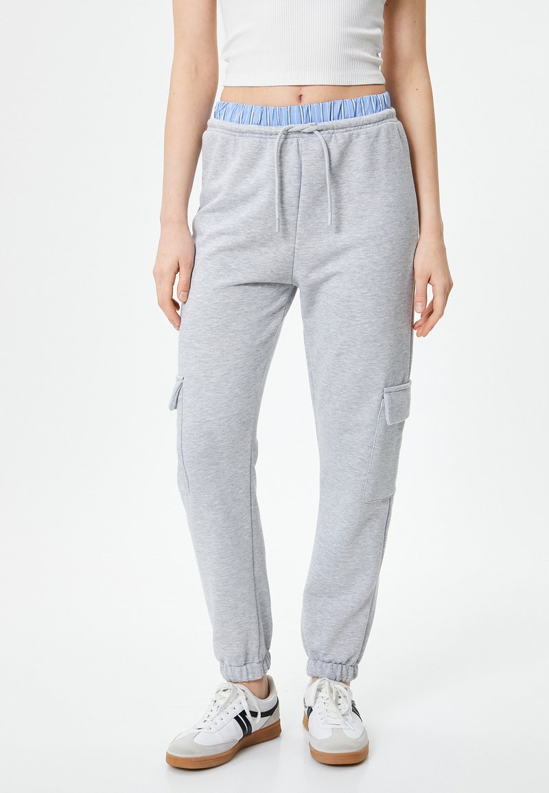 Graue Jogginghosen mit einem hellblauen elastischen Bund, Kordelzugverschluss, seitlichen Cargotaschen und schmal zulaufenden Bündchen, aus weichem, strukturiertem Stoff.