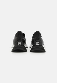 Svart sporty sneakers med en teksturert svart overdel, hvit såle og en fremtredende DKNY-logo på hælen. Flate snørebånd og løpehank inkludert.