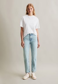 Witte katoenen t-shirt met korte mouwen, gecombineerd met lichtblauwe rechte jeans en witte sneakers met beige accenten. Eenvoudige zilveren ketting.
