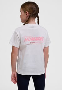 Weißes Baumwoll-T-Shirt mit großem pinkfarbenem "HUMMEL"-Logo und dem Text "EVERYDAY ACTIVE" auf dem Rücken. Kurze Ärmel, lässiger Schnitt.