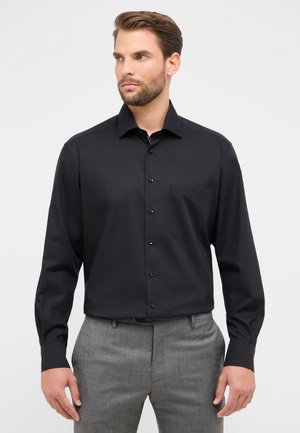 Zwarte overhemd met lange mouwen en een puntige kraag, voorzien van een borstzak en een gladde textuur. Gepaard met grijze broek.