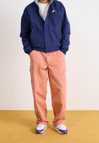 Marinblå vindjacka, grå krage, elastiska muddar; korallfärgade byxor; vita sneakers med lila detaljer. Enkel, avslappnad design, inga mönster.