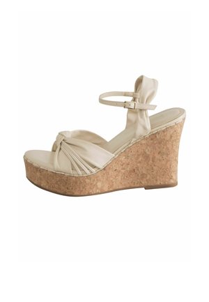 Beige wedge sandal featuring a knotted fabric upper, cork heel, and adjustable ankle strap. Smooth texture with stitched detailing.