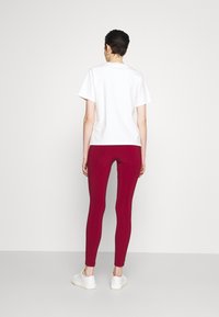 Biała koszulka z krótkim rękawem w połączeniu z czerwonymi legginsami, o dopasowanym kroju i gładkiej teksturze, uzupełniona białymi trampkami.