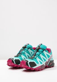 Leichte Trailrunning-Schuhe mit einem Obermaterial aus türkisfarbenem und schwarzem Mesh, pinken Akzenten, einem Schnell-Schnürsystem und einer strukturierten Gummisohle.