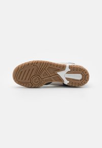 Schuhsohle mit braunem Profil, weißer Zwischensohle, gekennzeichnet mit "new balance" und "nicht abfärbender Sohle", vor einem schlichten weißen Hintergrund.