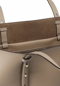 Beige leren handtas met een gladde afwerking, suède interieur en contrasterende handvatten met gespte accenten. Voorzien van een ritsvak.