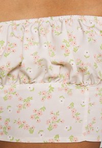 Top sem alças em tecido bege claro com decote franzido. Apresenta um padrão floral com flores cor-de-rosa e brancas e folhas verdes.