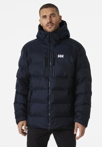 Chaqueta acolchada azul marino con cuello alto y capucha ajustable. Cuenta con dos bolsillos frontales, cierre de cremallera y logo "HH" en el pecho.