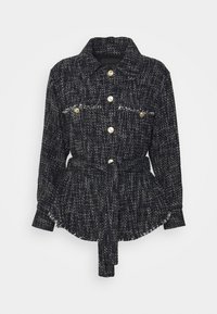 Veste texturée noire et blanche avec un col à revers, des boutons dorés en accent, deux poches à l'avant et une taille cintrée avec une ceinture.