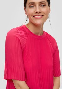 Fuchsia-gekleurde shirt met plooien, een ronde halslijn en korte mouwen. De stof heeft een gladde textuur en heeft verticale plooien over de gehele lengte.