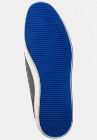 Semelle d'une chaussure avec un fond en caoutchouc bleu comportant des rainures horizontales, bordée de côtés blancs et gris pour la structure et l'adhérence.