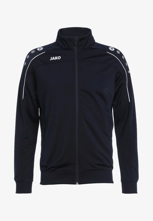 Marine blauw zip-up sportjack gemaakt van gladde stof, met witte accenten en ronde knopen op de schouders. Logo "JAKO" op de borst.