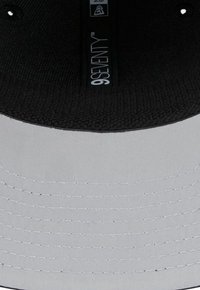 Schwarze und graue Kappe mit einem glatten Stoffäußeren, einem strukturierten Innenfutter und weißen Stichen entlang des gebogenen Schirms. Markiert mit "9SEVENTY."
