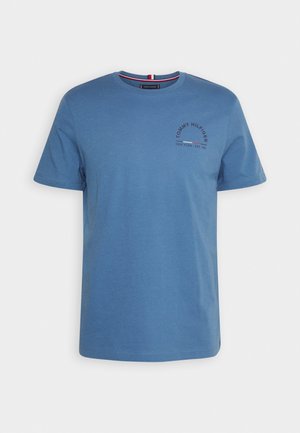 T-shirt en coton bleu avec col rond, manches courtes et un logo imprimé sur le côté gauche de la poitrine. Présente un accent rouge et blanc au niveau du col.