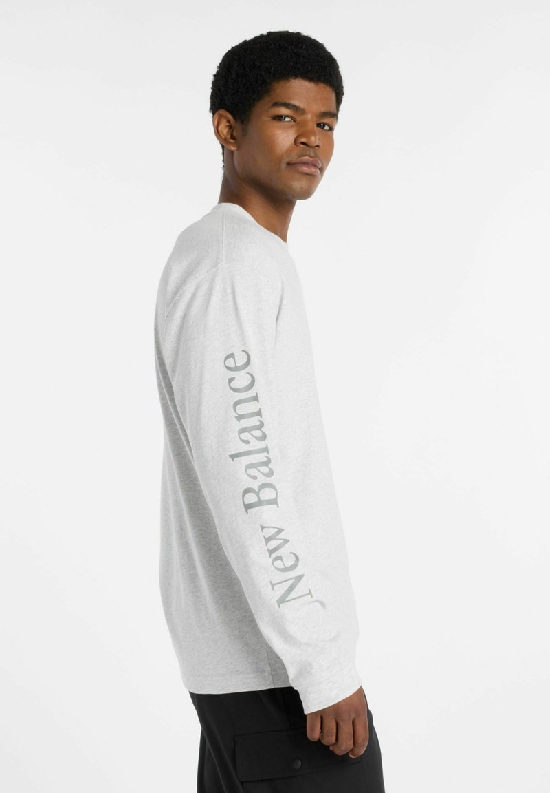 Long-sleeve gray t-shirt made of cotton, featuring "New Balance" logo in light gray on the left sleeve, crew neckline, and relaxed fit.