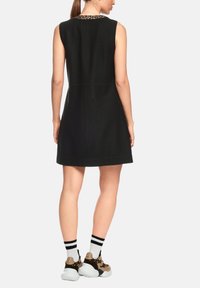 Schwarzes ärmelloses Kleid mit einem Leopardenmuster-Kragen. Es hat eine taillierte Silhouette und einen Saum oberhalb des Knies, kombiniert mit Sportschuhen und gestreiften Socken.