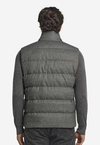 Graue Steppweste mit hohem Kragen, gesteppter Optik und matter Textur. Getragen über einem langärmligen grauen Shirt, das bis zur Taille reicht.