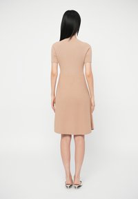 Vestido bege com riscas, mangas curtas, corpete ajustado, saia rodada e detalhes nas costas. Usado com sapatos de salto agudo, posicionado contra um fundo branco.