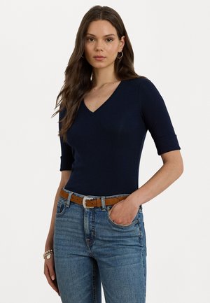 Haut bleu marine à col en V avec des manches courtes, design ajusté, texture douce, associé à un jean bleu clair et une ceinture brune avec une boucle en argent.