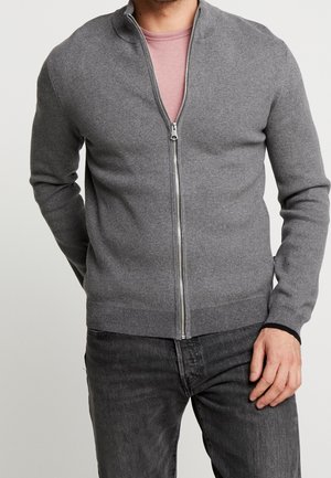 Gray zip-up sweater with a stand collar, ribbed cuffs and hem, made from a soft material, worn over a light pink t-shirt.