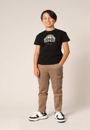 Zwarte katoenen t-shirt met een groen autografi, gecombineerd met beige cargo pants met zijzakken en zwart-witte sneakers.