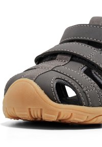 Grå sandal med åben tådesign, der har grå remme og en struktureret gummisål i tan. Synlige syninger og justerbare remme.