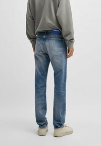 Ljusblå denimjeans med en avslappnad passform, med bakfickor och ett märkesband i midjan. Bärs med en grå sweatshirt och beige sneakers.