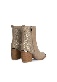 Botas de tobillo beige con un diseño recortado, que cuentan con una cremallera lateral, un patrón texturizado y un tacón de madera grueso. Diseño de punta abierta en la parte frontal.