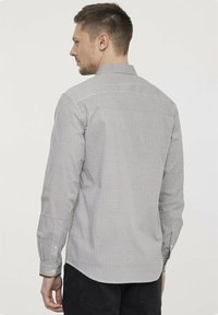 Chemise grise et blanche avec un motif géométrique, dotée de manches longues et d'un col boutonné. Texture lisse et coupe ajustée.