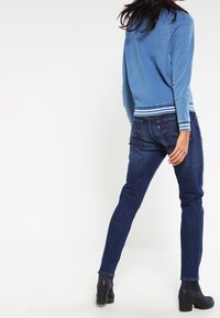 Sininen neule, jossa raidalliset hihansuut, yhdistetty tummansinisiin farkkuihin. Asusteessa on suora leikkaus ja mustat nilkkasaappaat.