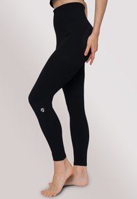 Leggings neri a vita alta realizzati in tessuto elasticizzato, con una texture liscia e un piccolo logo bianco vicino alla caviglia.