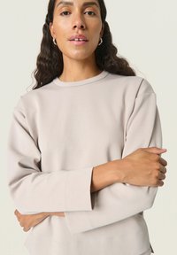 Lys beige sweatshirt med lange ærmer, rund halsudskæring og synlige sømdetaljer. Glat tekstur, afslappet pasform og enkelt design.