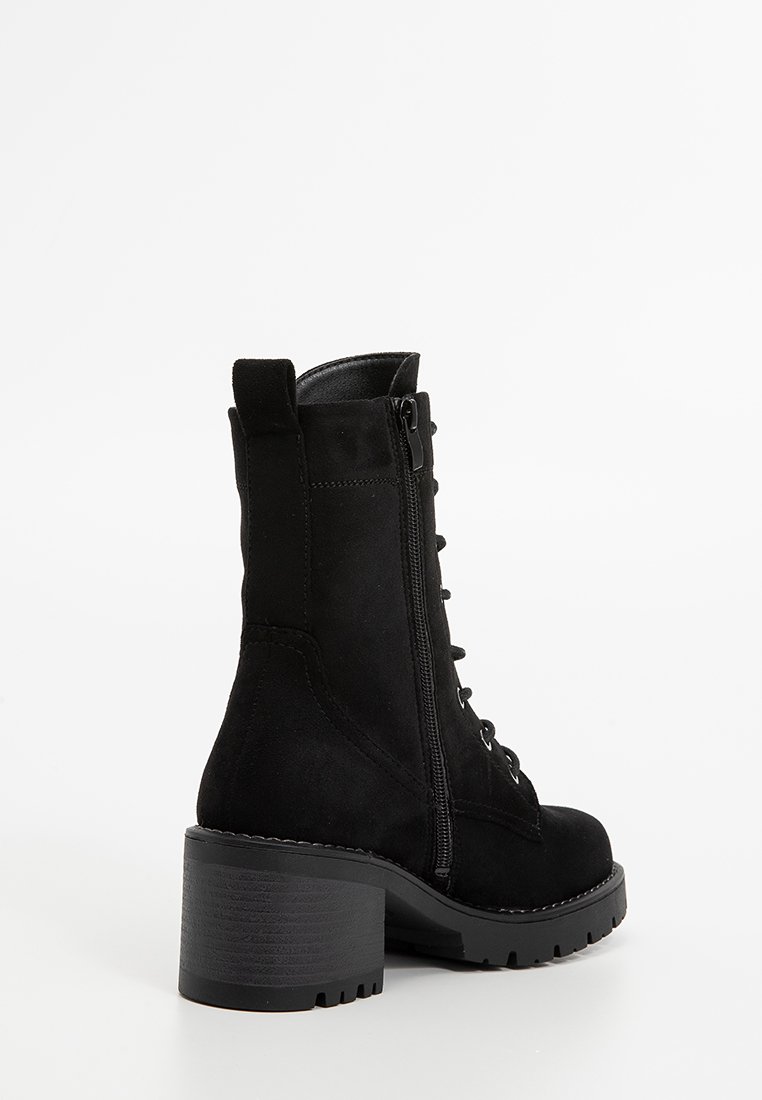 Botín de tobillo de ante negro con tacón cuadrado, que presenta un cierre lateral con cremallera, un frente con cordones y una suela texturizada para mayor agarre.
