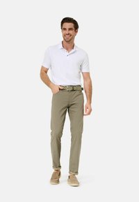 Witte poloshirt, kaki broek, gemusterde riem, beige instappers. Casual outfit met opgerolde manchetten op de broek, rechte pasvorm.