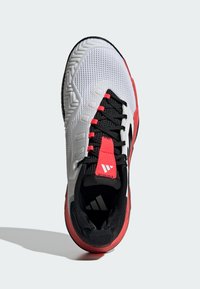 Weißer Sportschuh mit strukturiertem Obermaterial, schwarzen Akzenten und roten Details. Verfügt über ein Schnürdesign und eine strapazierfähige Gummisohle.