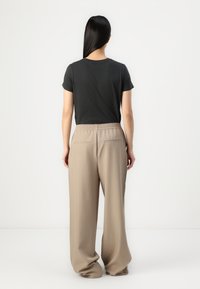 T-shirt noir ajusté à manches courtes associé à un pantalon large beige, doté d'une taille élastique et de poches arrière.