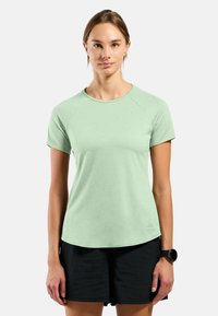Light green short-sleeve athletic shirt with a round neck, smooth texture, and raglan sleeves, paired with black shorts.