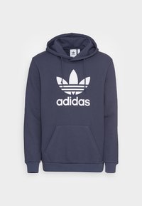 Sudadera azul marino hecha de una mezcla de algodón, con un gran logo trefoil blanco de Adidas y un bolsillo tipo canguro en la parte delantera. Capucha ajustable.