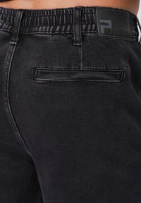 Μαύρο παντελόνι από τζιν με ελαστική μέση, με πίσω τσέπη και ετικέτα λογότυπου στη μέση. Μαλακή υφή και δομημένος σχεδιασμός.