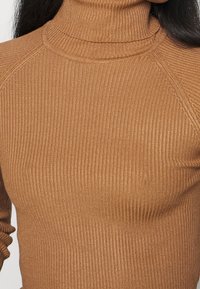 Zbliżenie osoby noszącej dopasowany, prążkowany, wielbłądzi golf z długimi rękawami.