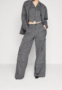 Szary trzyczęściowy zestaw składający się z skróconego kamizelki, luźnych spodni z kieszeniami cargo i dopasowanej marynarki. Teksturowany materiał z detalami w postaci guzików.