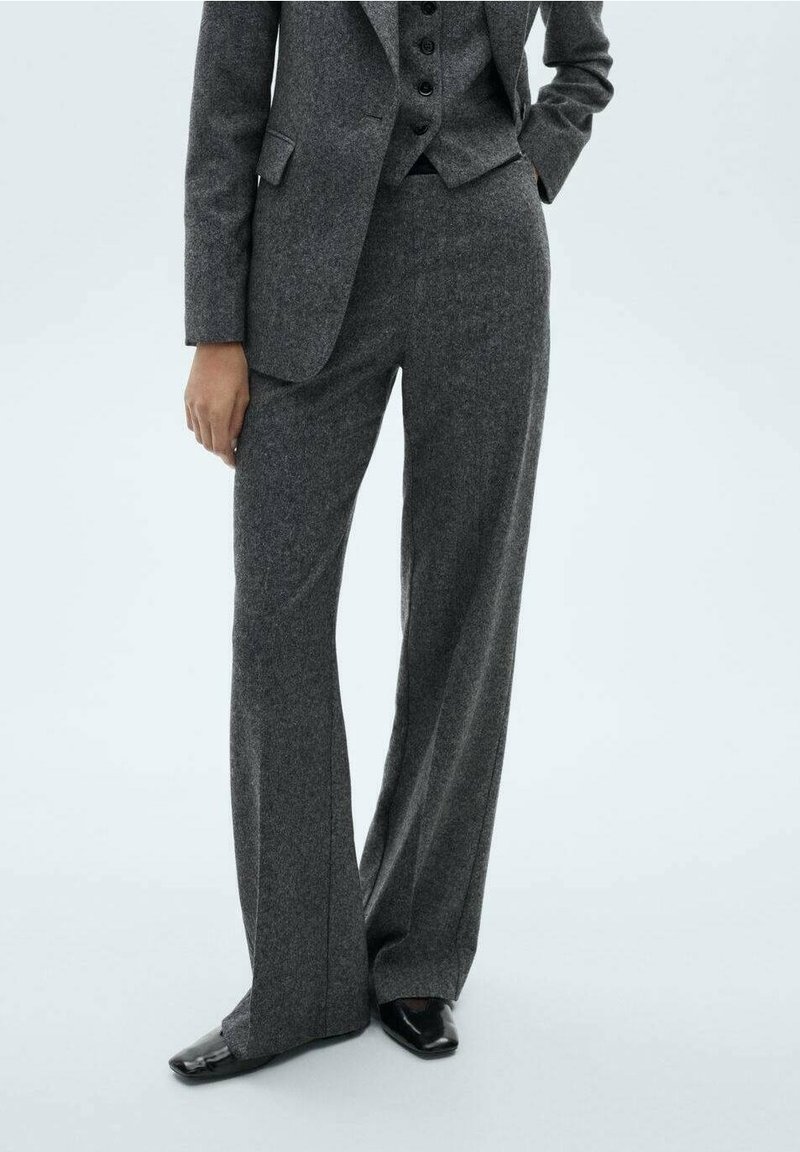 Grijze op maat gemaakte pak met wijde broekspijpen, gestructureerde stof en een getailleerde blazer. Voorzien van knopen op het vest en elegante zwarte schoenen.